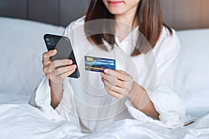 Woman using mobile smart phone and credit card for online shopping while making order on bed in morning at home. technology,