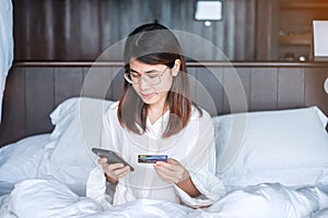 Woman using mobile smart phone and credit card for online shopping while making order on bed in morning at home. technology,