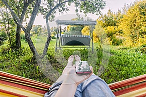 Woman using mobile smart phone and relaxing in a hammock in summer garden