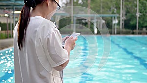 Woman using mobile smart phone texting messages at swimming pool.