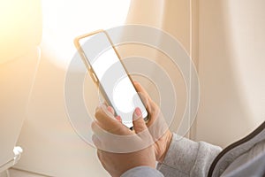 Woman using mockup smartphone on airplane. woman`s hands holding a black smart phone with blank desktop screen next in the cabin