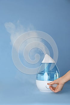 Woman using modern air humidifier on blue background, closeup