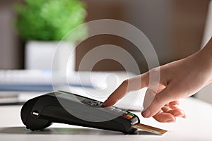 Woman using modern payment terminal at table indoors, closeup.