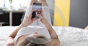 Woman using modern smartphone looks through photos from relaxing on bed at home closeup