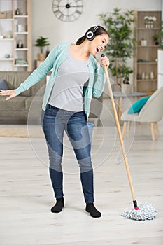 woman using mop as micophone and singing while doing housework