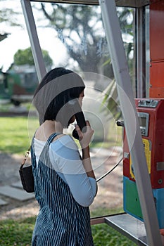 Woman using oldstyle public pay phone in telephone booth