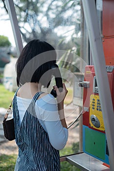 Woman using oldstyle public pay phone in telephone booth