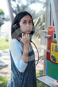 Woman using oldstyle  public pay phone in telephone booth