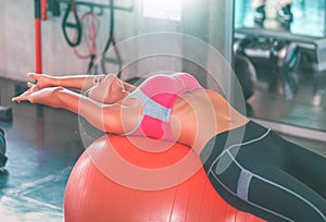 Woman using orange fitness ball to stretch her back and exercise her abs in fitness gym workout room