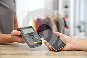 Woman using payment terminal with smartphone in shop