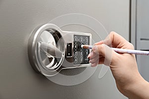 Woman using pencil to enter code on keypad of safe, closeup