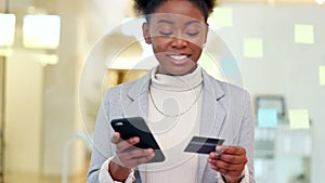 Woman using a phone and bank card to make an online payment, standing in an office. Young african business woman typing