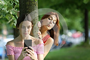 Woman using phone being spied by her friend