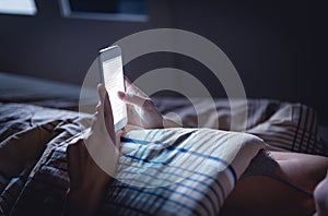 Woman using phone late at night in bed. Person looking at text messages with cell in dark home. Hipster online dating or texting.