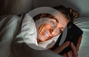 Woman using phone late at night in bed. Person taking selfie for a Online dating app with cell in dark home. Sexting or cheating