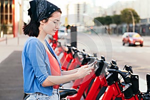 Woman using phone next to a bike rental station