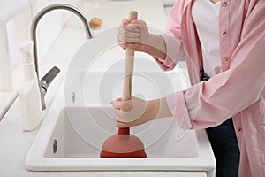Woman using plunger to unclog sink drain in kitchen, closeup