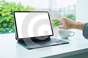 A woman using and pointing finger at digital tablet with blank desktop white screen as a computer pc in office