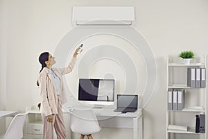 Woman using remote control to switch wall air conditioner in modern office workplace