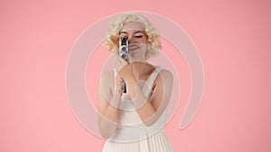 Woman using retro video camera close up. Woman looking like Marilyn Monroe in studio on pink background.