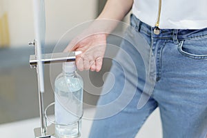 Woman using sanitiser dispenser foot pump.  Hand free alcohol hand gel dispenser. Stop Coronavirus Covid-19 Spread