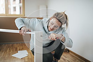 Woman using screwdriver for assembling furniture at home