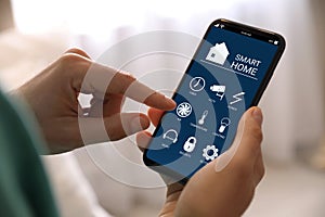 Woman using Smart Home app on mobile phone indoors, closeup