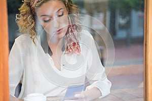 Woman using smart phone in cafe seen through window