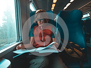Woman using smart phone sitting traveling by train hand writing on paper. Desaturated cold tone color grading. Working mobility co