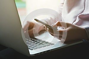 Woman using smart phone, touching screen and working on laptop