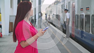 Woman using smart phone while waiting train as arrival. Using Travel App or Checking Train Schedule