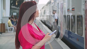 Woman using smart phone while waiting train as arrival. Using Travel App or Checking Train Schedule