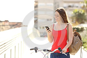 Woman using a smart phone walking with a bicycle