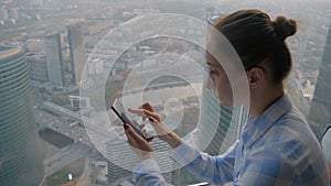 Woman using smartphone against cityscape view through window of skyscraper