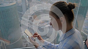 Woman using smartphone against cityscape view through window of skyscraper