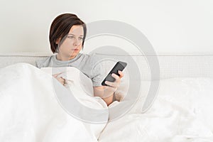 Woman using smartphone as she sits in bed covered with duvet