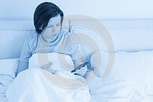 Woman using smartphone as she sits in bed covered with duvet