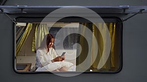 Woman using smartphone on bed of a camper RV van motorhome at night