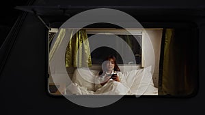 Woman using smartphone on bed of a camper RV van motorhome at night
