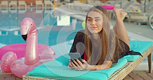 Woman using smartphone on a chair at swimming pool.