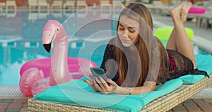 Woman using smartphone on a chair at swimming pool.
