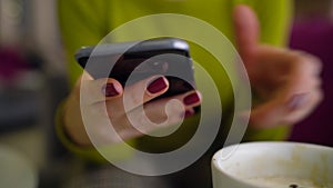 Woman using smartphone and drinking coffee in cafe close up