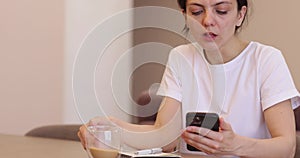 woman using a smartphone and drinking coffee i the kitchen