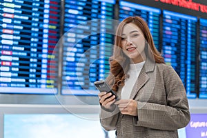 Woman using smartphone with flight information board at airport