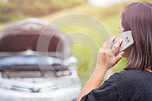 Woman using smartphone in front of her broken car on the road. C