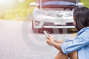 Woman using smartphone in front of her broken car on the road. C