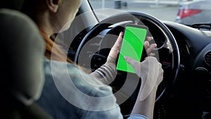 A woman using a smartphone with a green screen in her hand driving a car. Chroma key.