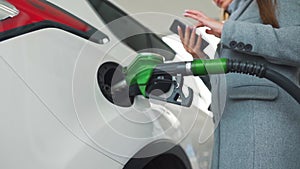 Woman using smartphone while her car is refueling. Slow motion