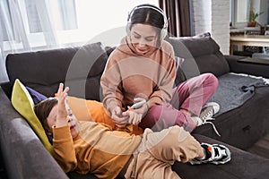 Woman using smartphone while her cute son with down syndrome laying at the sofa nearby