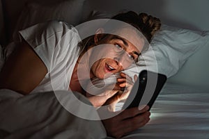 Woman using smartphone late at night in bed. Person looking at Online dating app photos from man with cell in dark home. Sexting